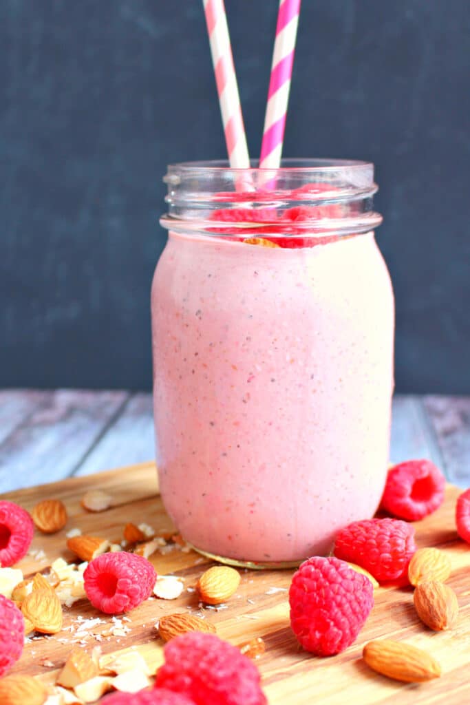 Raspberry Almond chia smoothie with two straws and garnished with fresh raspberries and almonds.