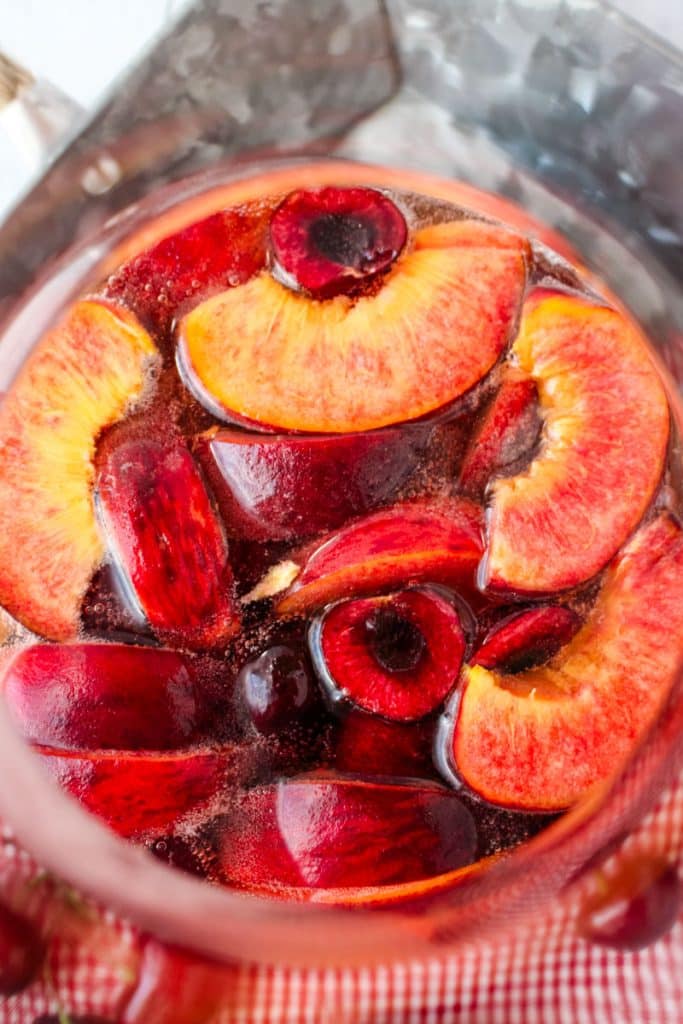 Fresh peach sangria with cherries in a large pitcher.