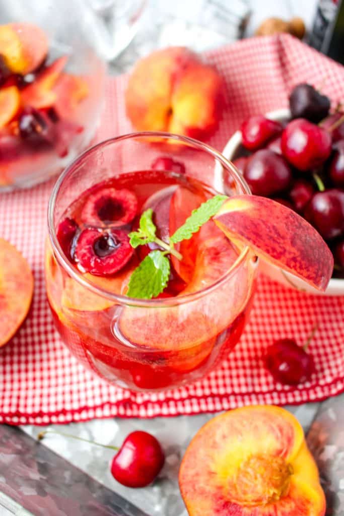 Prosecco sangria with fresh peach slices and cherries, topped with fresh mint leaves.