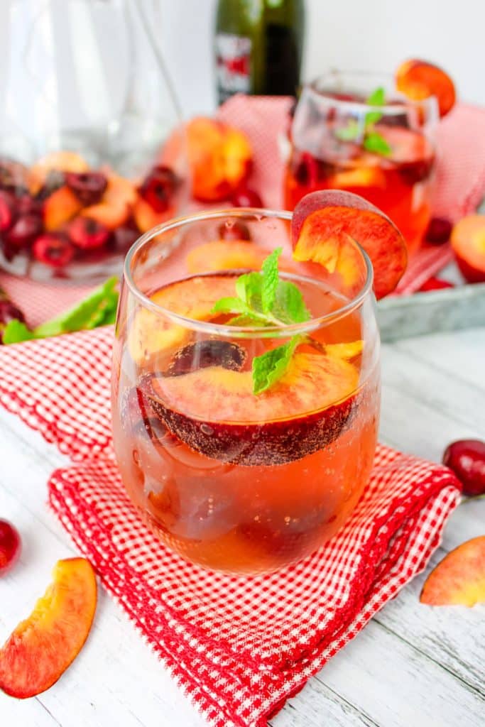 Glass of prosecco sangria with fresh peaches and cherries topped with fresh mint leaves.