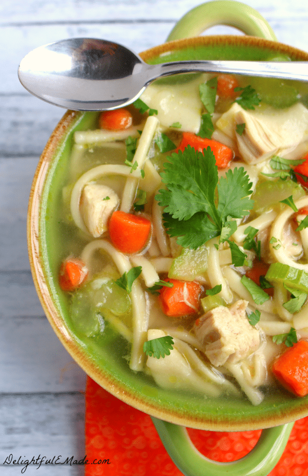 Hearty chicken noodle soup in a bowl, with spoon resting on side of bowl.