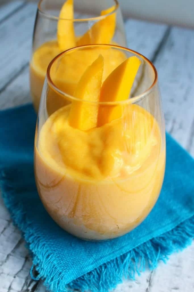 Healthy mango peach smoothie topped with mango slices and sitting on a blue napkin.