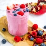 Pomegranate smoothie in glass topped with fresh berries.