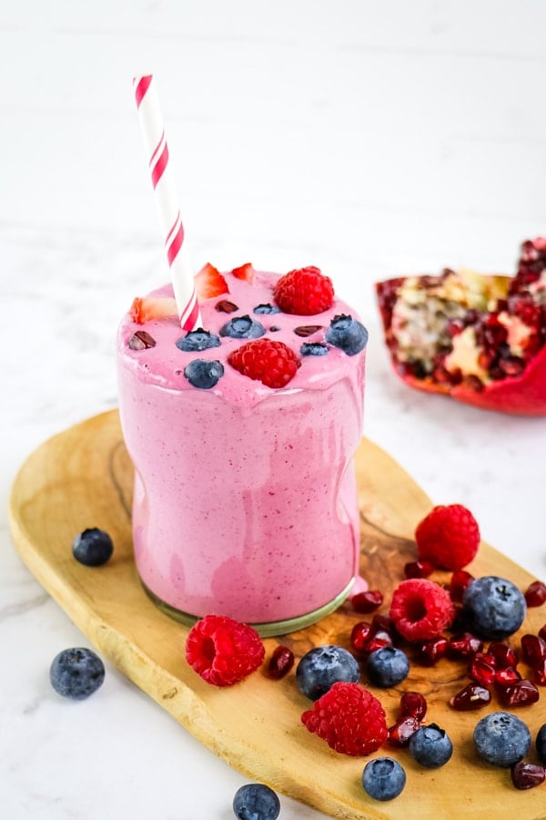 Pomegranate smoothie in glass with straw, and garnished with fresh berries and pomegranate arils.