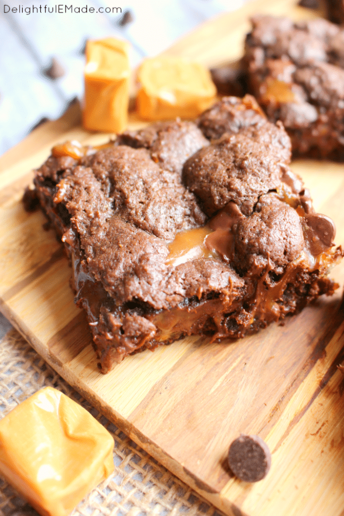 Cake mix turtle brownies on board, garnished with chocolate chips and caramels.