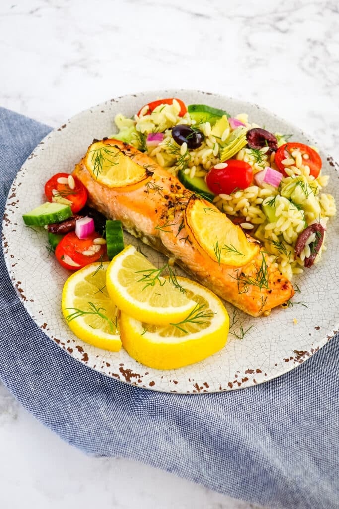 Grilled salmon on a plate with orzo salad and sliced lemons.