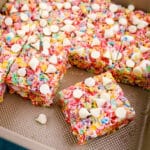 Fruity pebbles treats recipe in a pan, with treats cut into squares and topped with white chocolate chips.