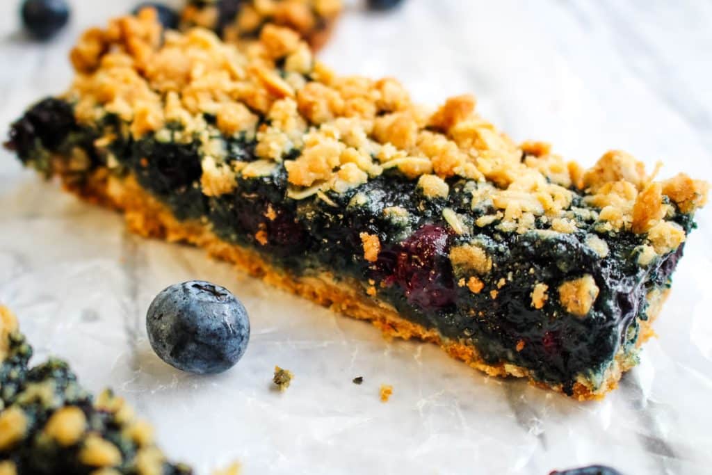 Single blueberry oatmeal bar cut into a long slice, and garnished with fresh blueberries.