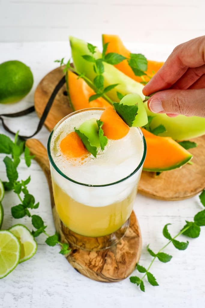 Mojito being garnished with a spear of melon balls and mint leaves.