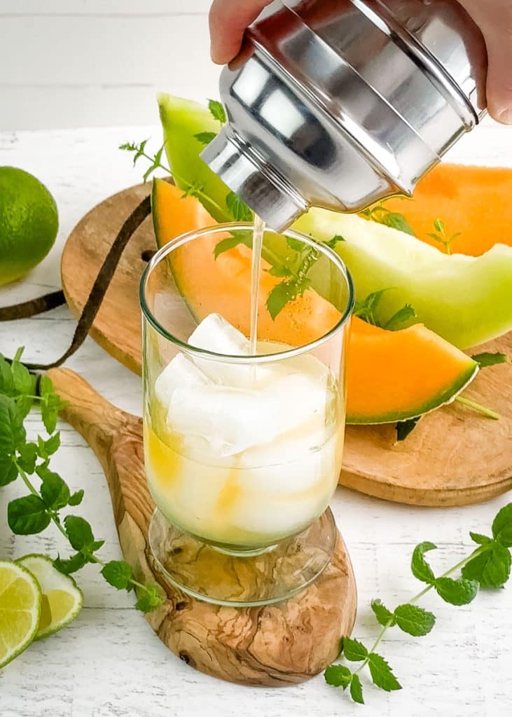 Melon mojito being poured over ice in a glass.