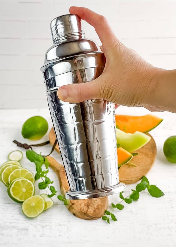 A silver cocktail shaker being shaken with a hand.