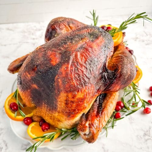 Roasted turkey on a platter garnished with orange slices, cranberries and rosemary sprigs.