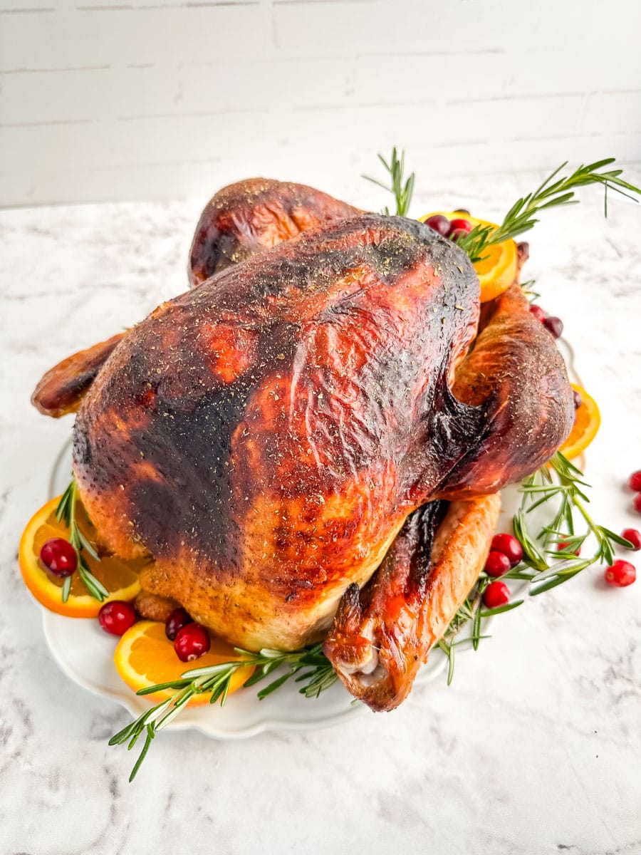 Roasted turkey on a platter garnished with orange slices, cranberries and rosemary sprigs.
