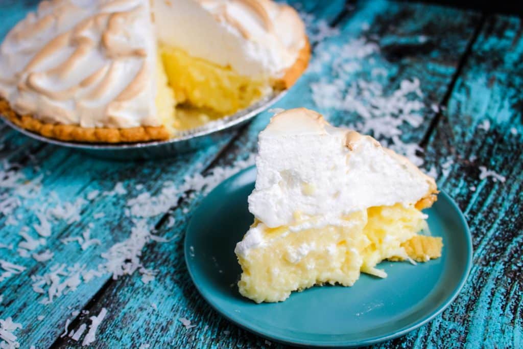 Slice of coconut cream pie on a plate with full pie in the background.