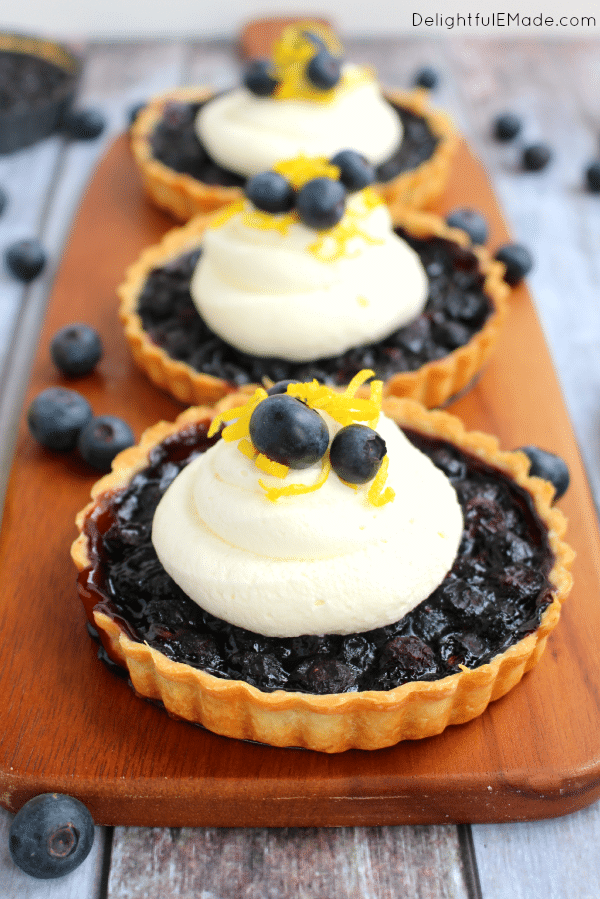 Three blueberry tarts topped with mascarpone cream, lemon zest and fresh blueberries.