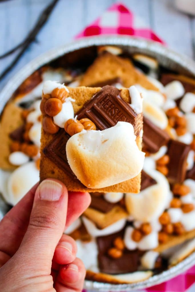 Single smores nacho held in hand over the top of the smores in pan.