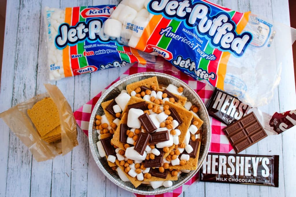 Ingredients needed to make smores in pan, including marshmallows, Hershey's bars, graham crackers and caramel bits.