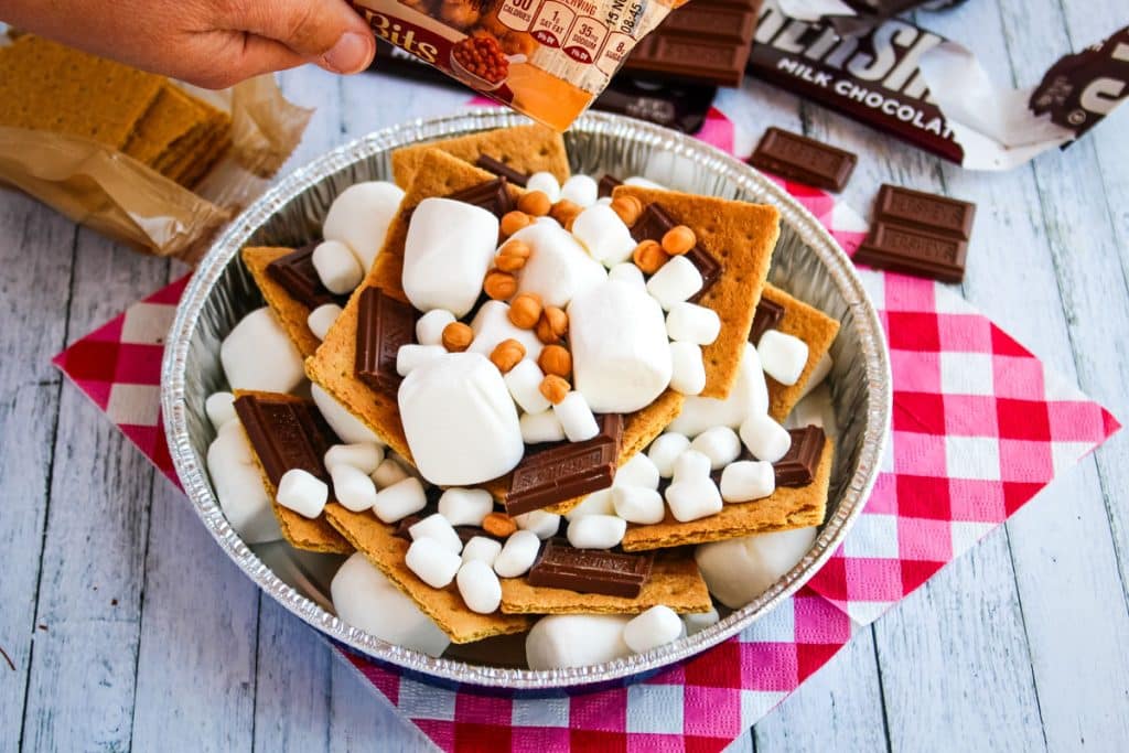 Campfire smores in pan with marshmallows, chocolate bars, graham crackers and caramel bits.