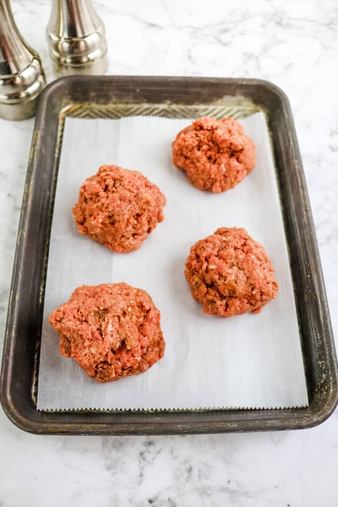 Ground beef mixture separated into balls for pressing into burger patties.