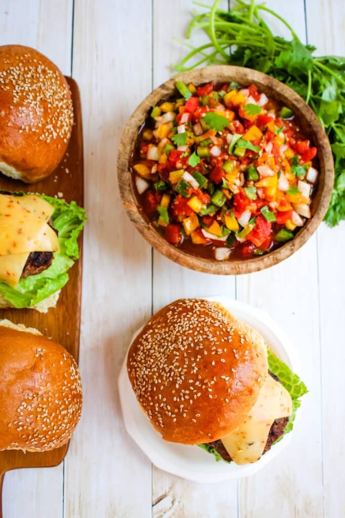 Burger with salsa bowl on the side, burgers on buns with cheese and luttuce.