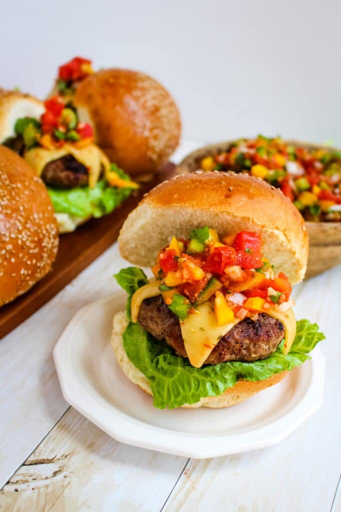 Burger with salsa and pepper jack cheese with bowl of salsa and extra burgers in the background.