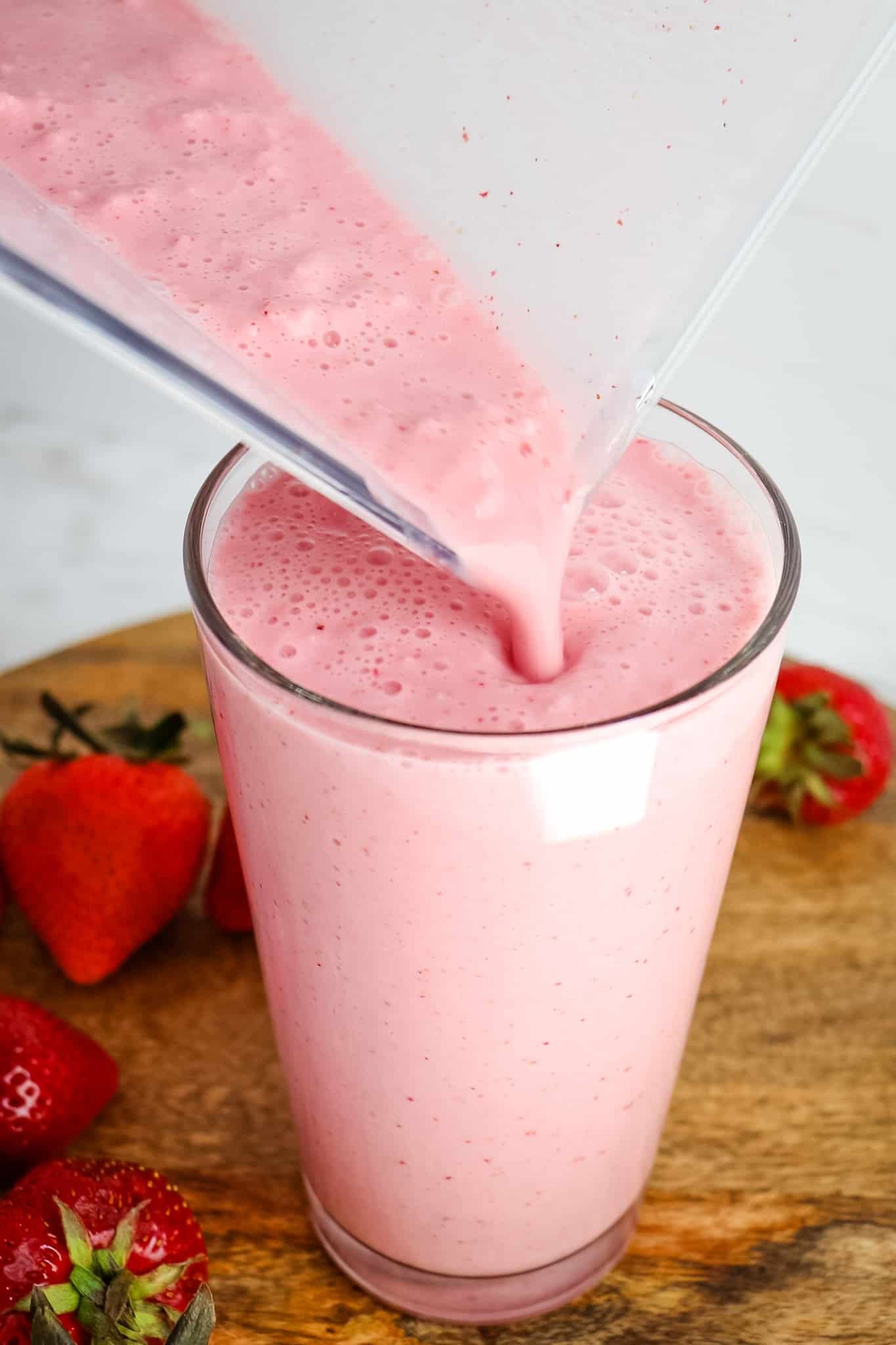 Pouring strawberry frappe into a glass from a blender pitcher.