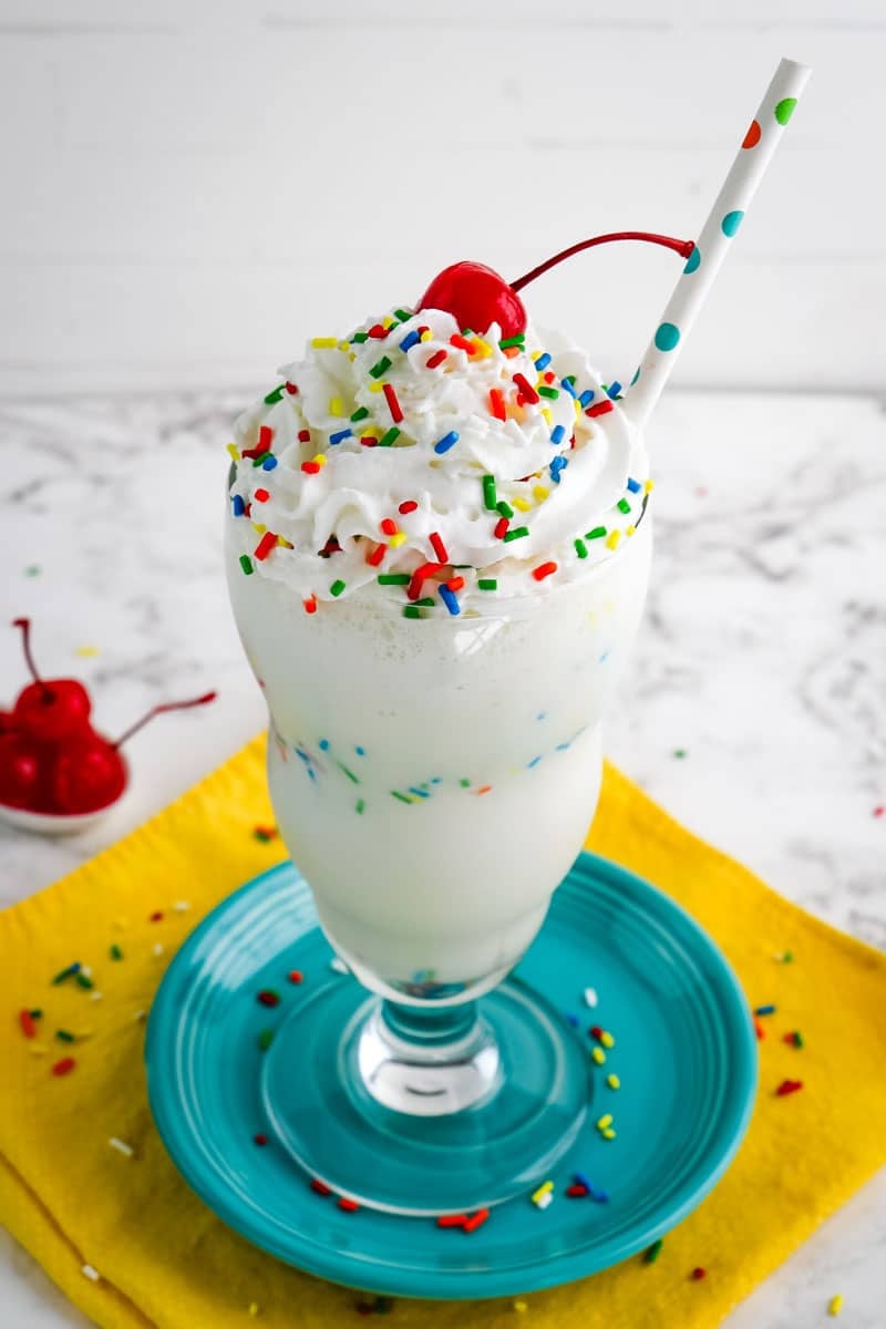Vanilla milkshake with sprinkles topped with whipped cream, extra sprinkles and a maraschino cherry.