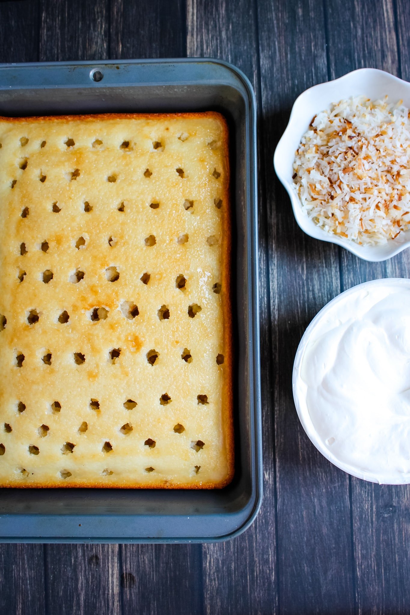 Coconut cake with holes, whipped cream and toasted coconut on the side.