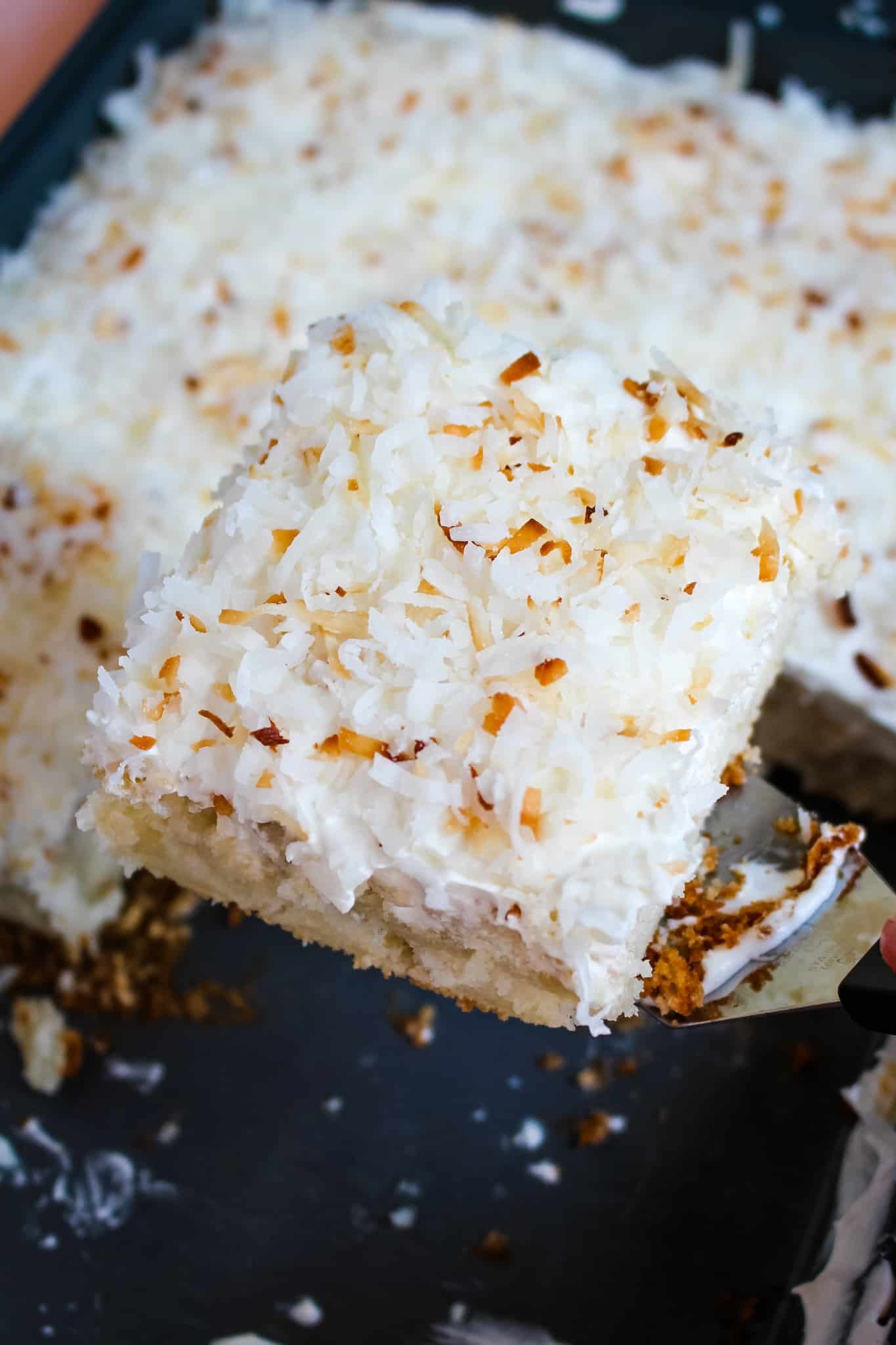 Slice of coconut poke cake being lifted out of pan.