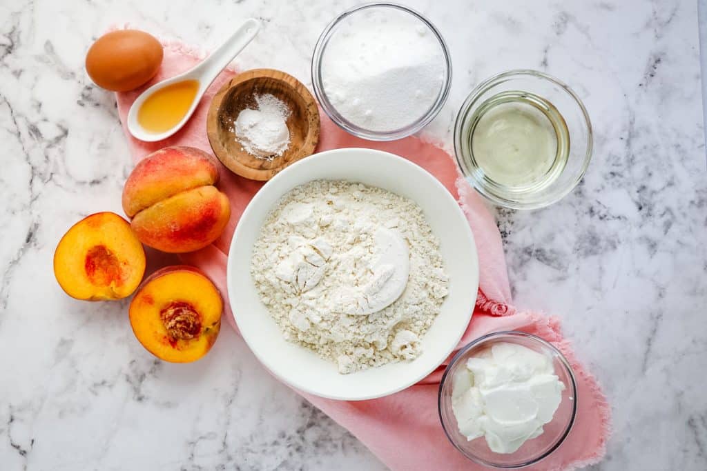 Ingredients to make a peach coffee cake, fresh peaches, wet ingredients and dry ingredients.
