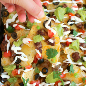 Loaded steak nachos on a sheet pan, topped with sour cream, cilantro, olives and tomatoes.