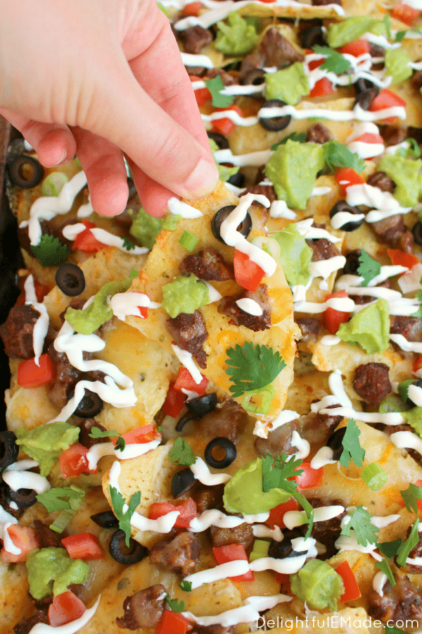 Loaded steak nachos on a sheet pan, topped with sour cream, cilantro, olives and tomatoes.