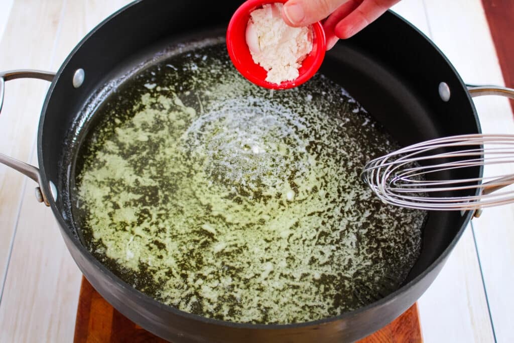 Flour being added to melted butter in a large skillet for making homemade alfredo sauce.