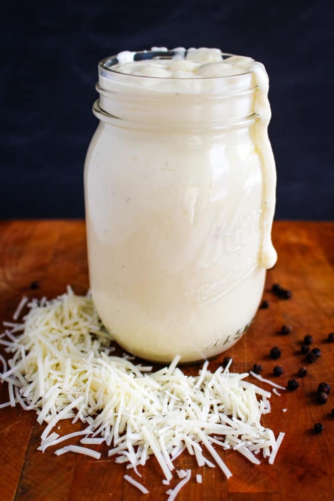 Homemade Alfredo sauce in a jar with shredded cheese on the side.