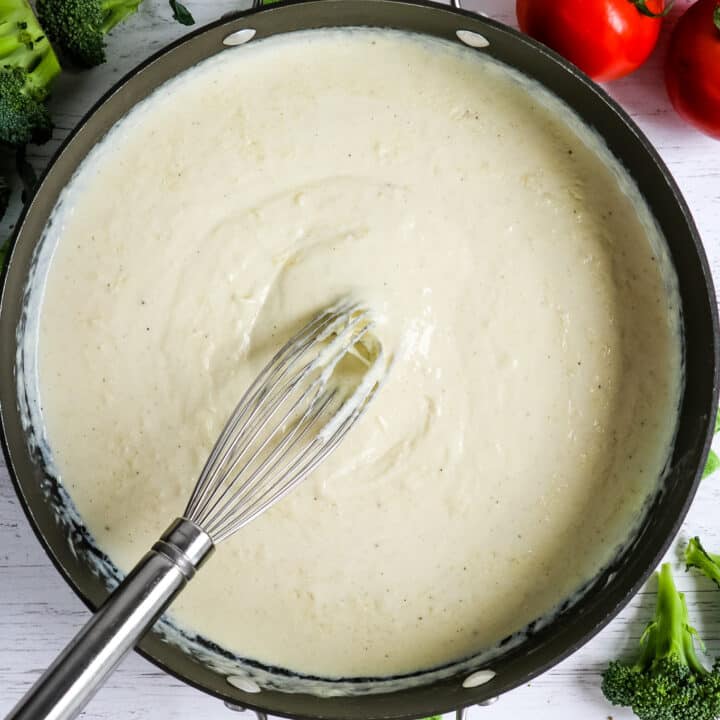 Homemade alfredo sauce in a skillet with a whisk in the center.
