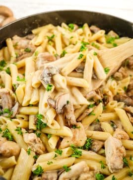 Creamy chicken and mushroom pasta being spooned out of the skillet with a wooden spoon.