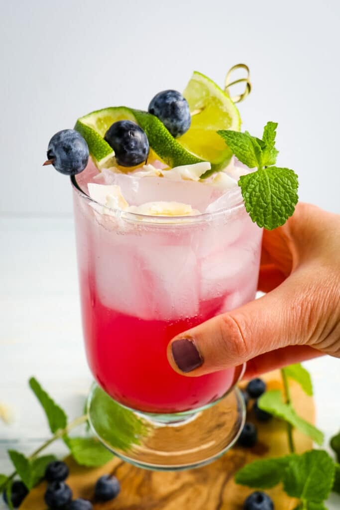 Blueberry mojito in a glass and topped with mint limes and blueberries.