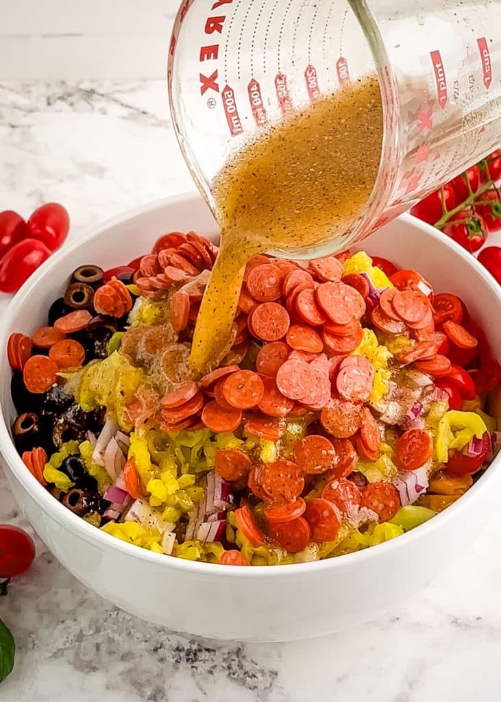 Italian dressing being poured over ingredients for pasta salad.