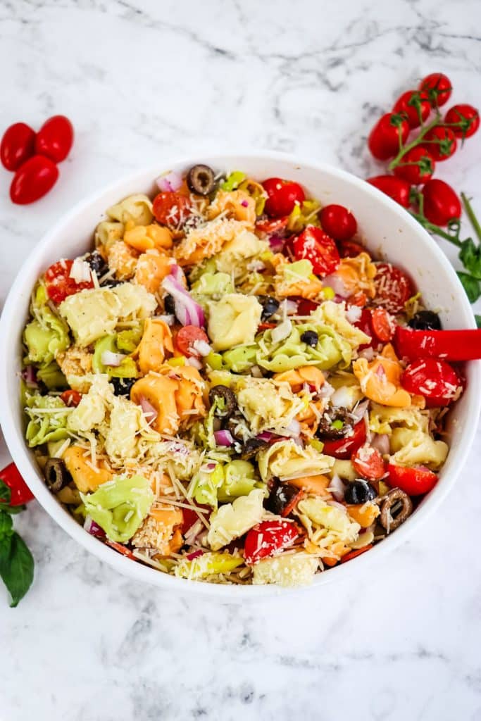 Italian tortellin salad being mixed together with a rubber scraper.