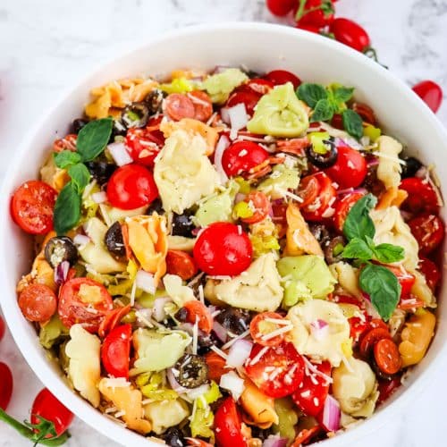 Italian tortellini pasta salad in a large white bowl garnished with basil leaves and tomatoes.