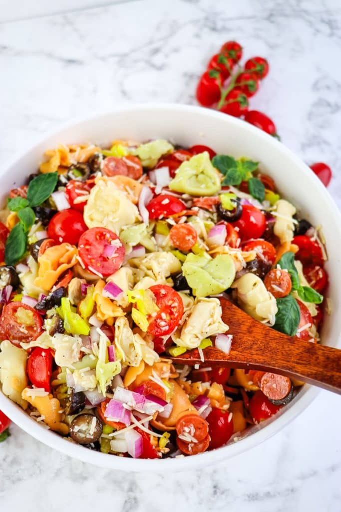 Italian tortellini pasta salad in a serving bowl with a wooden serving spoon.