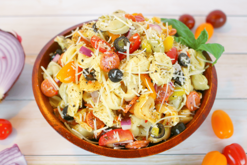 The perfect pasta salad or side dish for any pot-luck, picnic, cookout or backyard barbecue! This delicious tortellini salad is loaded with all of your Italian favorites, like salami, tomatoes, olives, banana peppers, red onion, and topped with Italian dressing and shredded Parmesan cheese! 