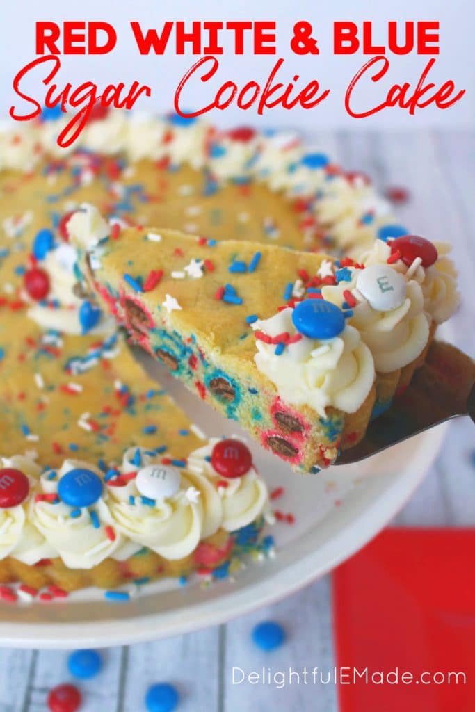 Red, white and blue sugar cookie cake decorated with vanilla frosting, red, white and blue M&M candies and sprinkles. Slice of cookie cake being lifted out of cake.