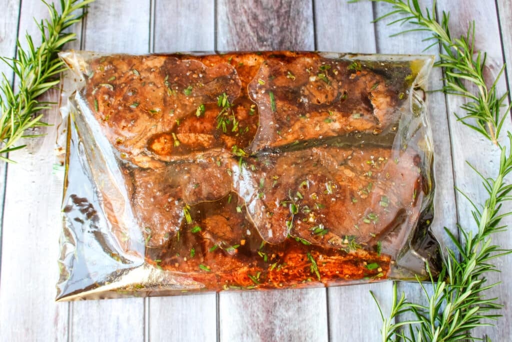 Steaks and balsamic steak marinade in a clear resealable bag with sprigs of rosemary on the side.
