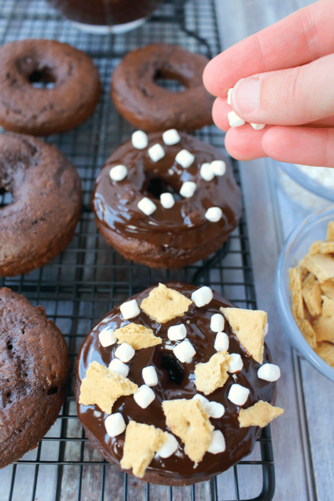 The classic campfire snack turned into a breakfast treat! These delicious Chocolate S'mores Donuts are simply baked in a donut pan, topped with a chocolate ganache frosting and sprinkled with marshmallows and graham crackers! These will be a new favorite anytime you're in the mood for something sweet!