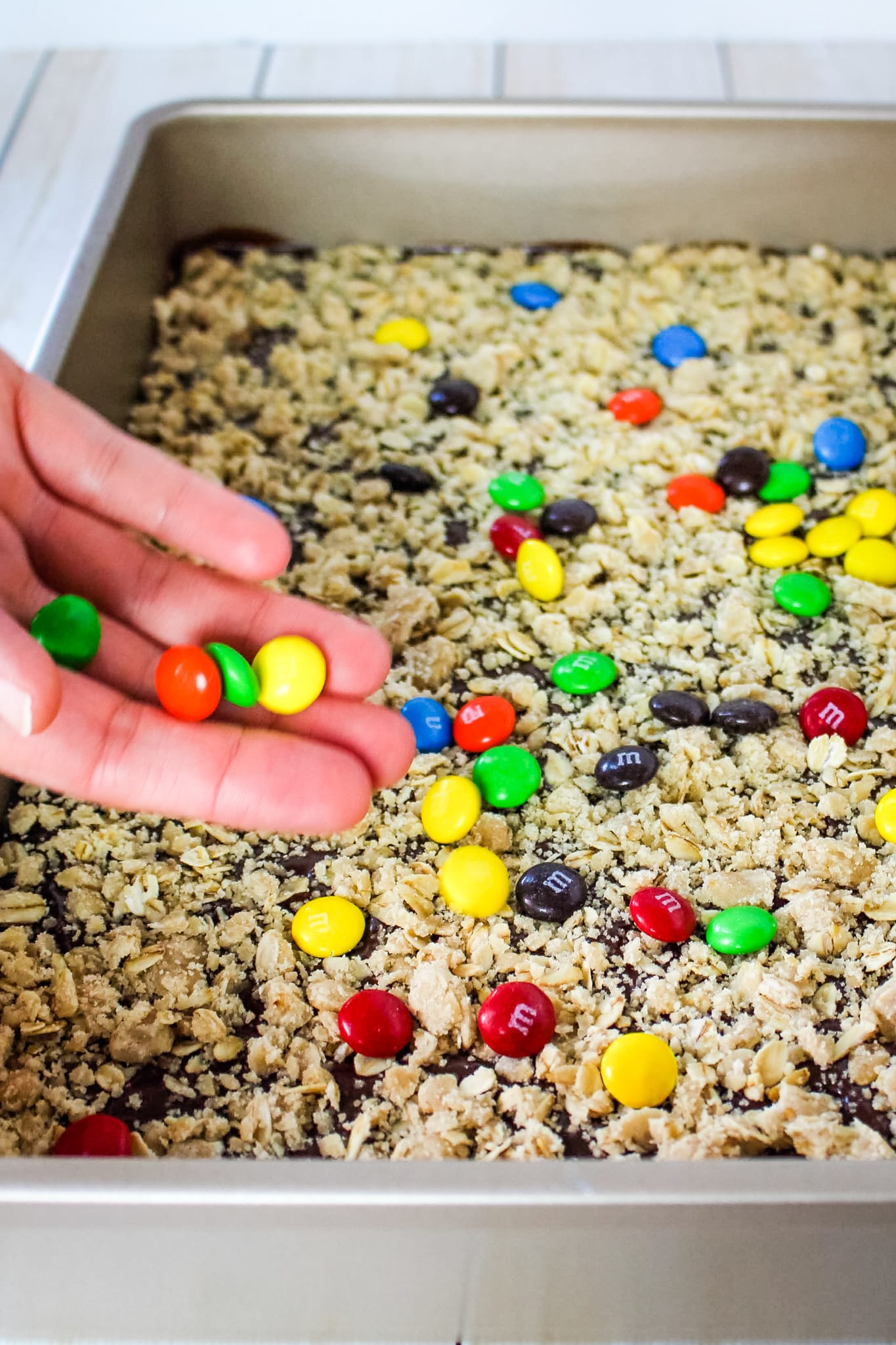 M&M oatmeal cookie bars, M&M candies being sprinkled over top of the oatmeal crumble.
