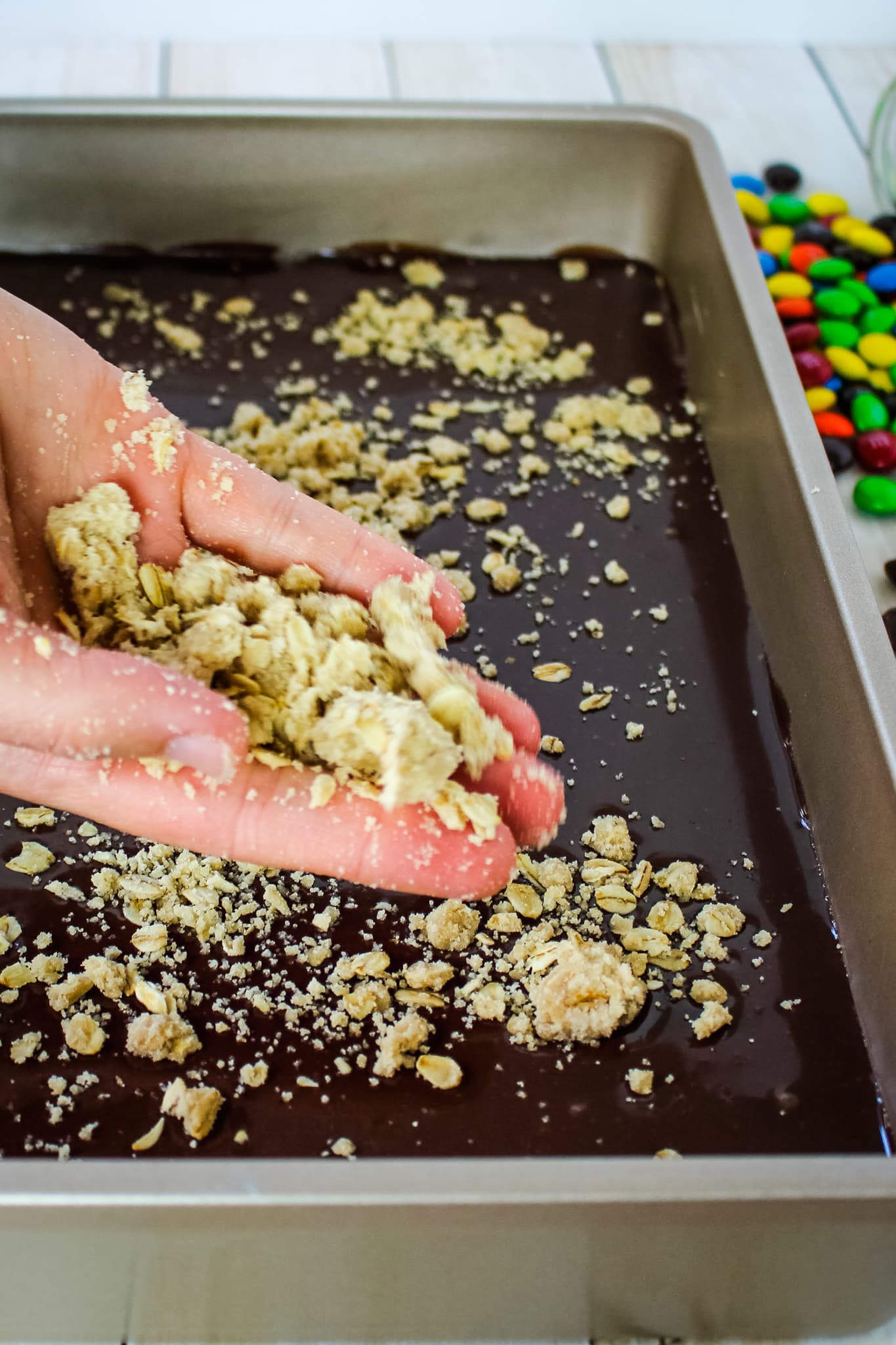 M&M oatmeal cookie bars, Oatmeal crumble being sprinkled on top of chocolate filling.
