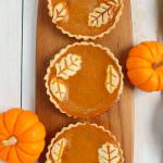 Three pumpkin pie tarts garnished with pumpkins on the side.