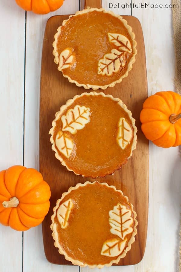 Three pumpkin pie tarts garnished with pumpkins on the side.