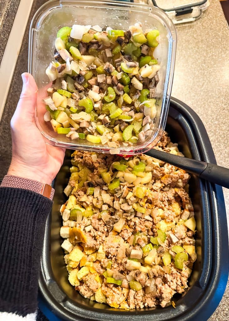 Sauted vegetables being added to stuffing cubes into slow cooker.